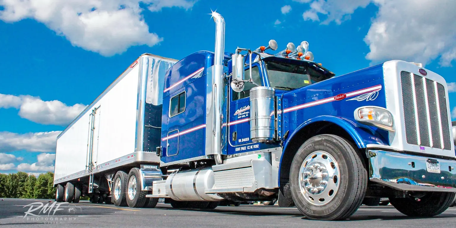 Blue Peterbilt tractor and trailer beneath a vivid sky
