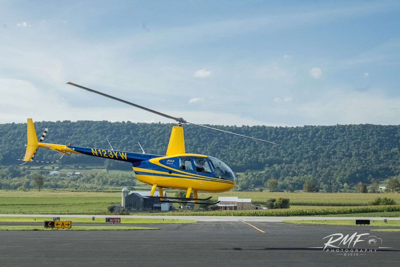 Yellow and blue Robinson helicopter hovering above a Central Pennsylvania airfield