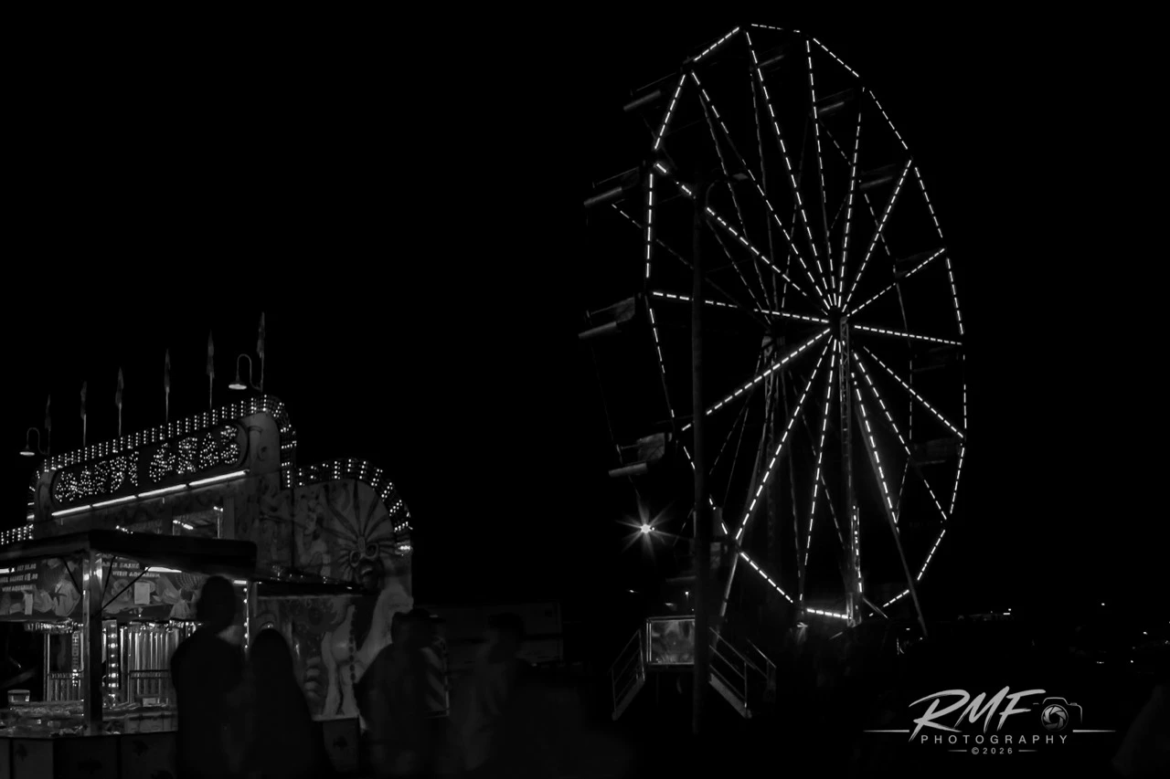 Black-and-white Ferris wheel and midway attraction photographed at night