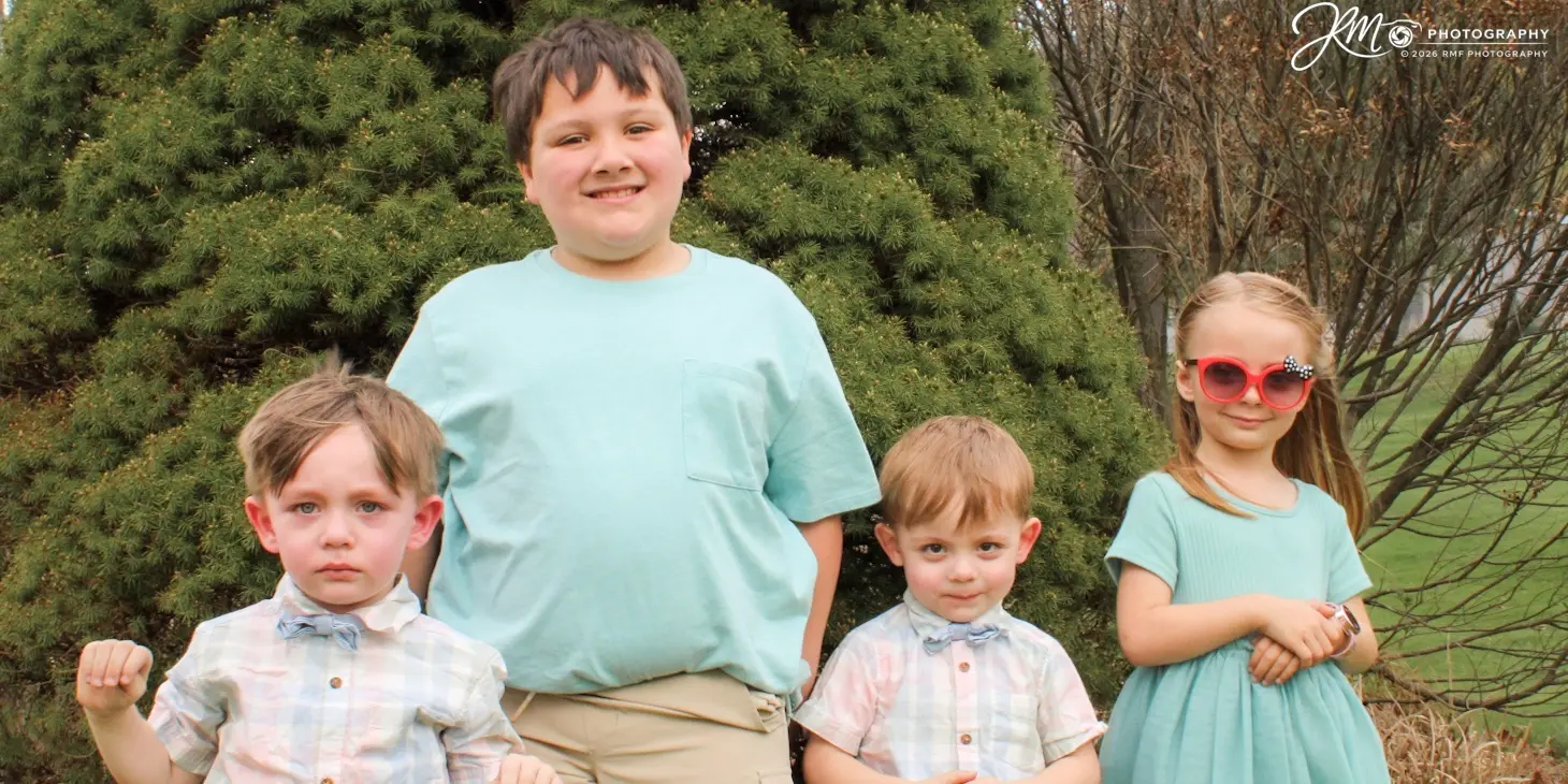 Four siblings standing together beside evergreen trees
