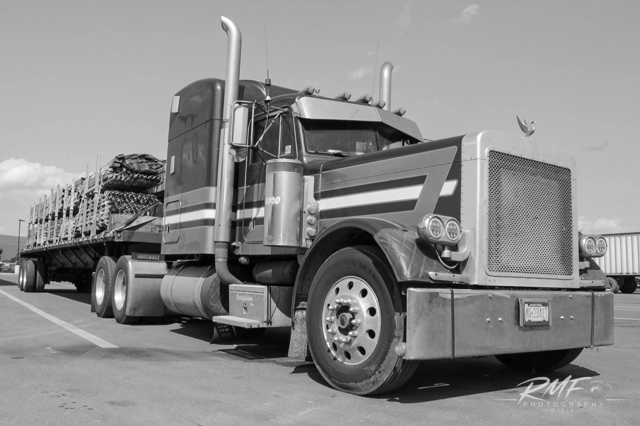 Black-and-white portrait of a classic long-nose tractor and loaded flatbed