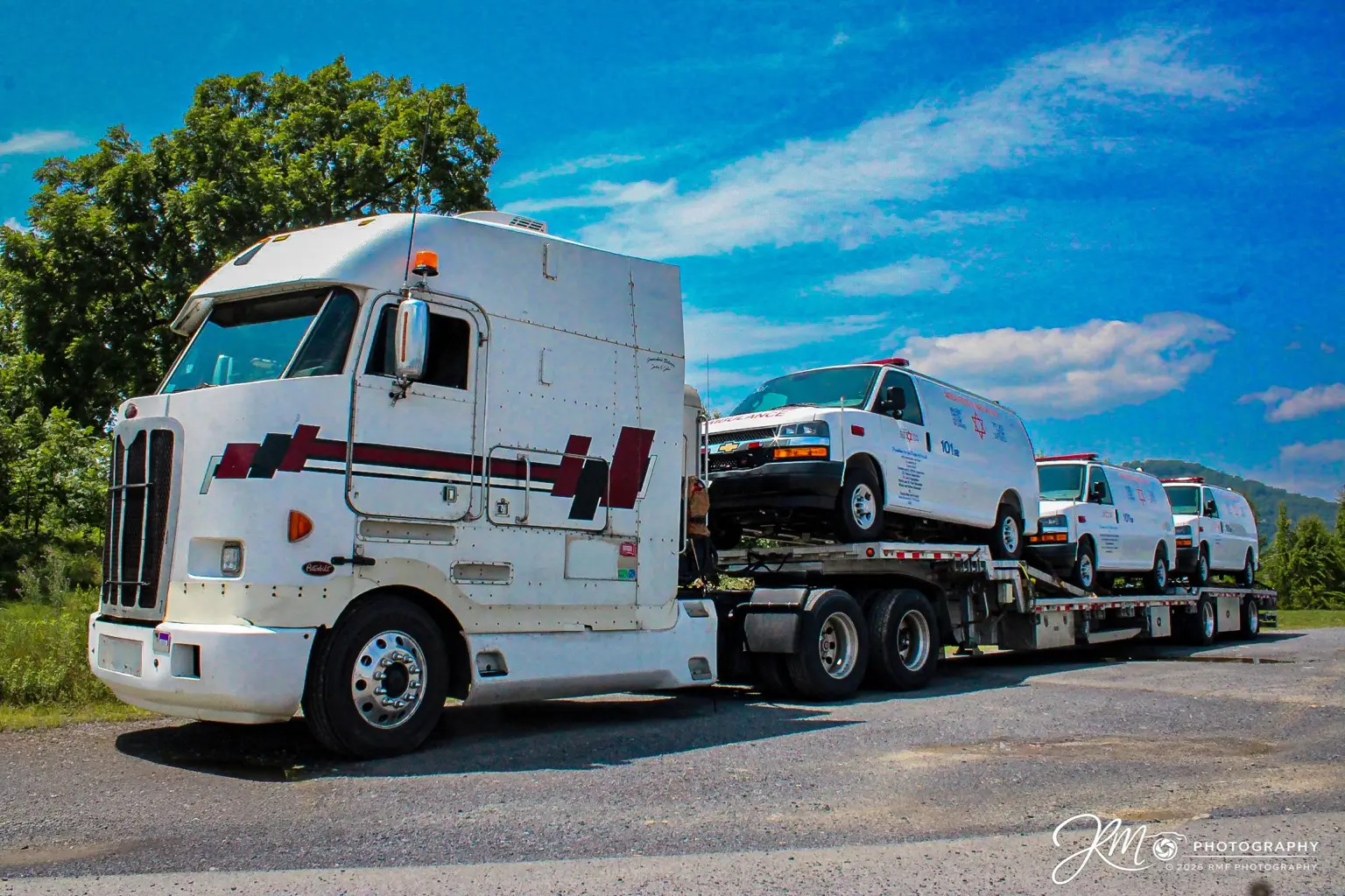 White Peterbilt cabover transporting a fleet of medical service vans